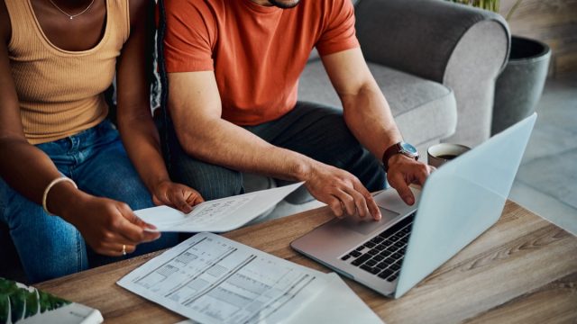 Cropped shot of an unrecognisable couple sitting in the living room and using a laptop to calculate their finances