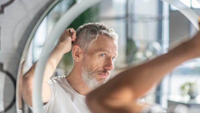 A middle aged man with salt and pepper hair looking in the mirror
