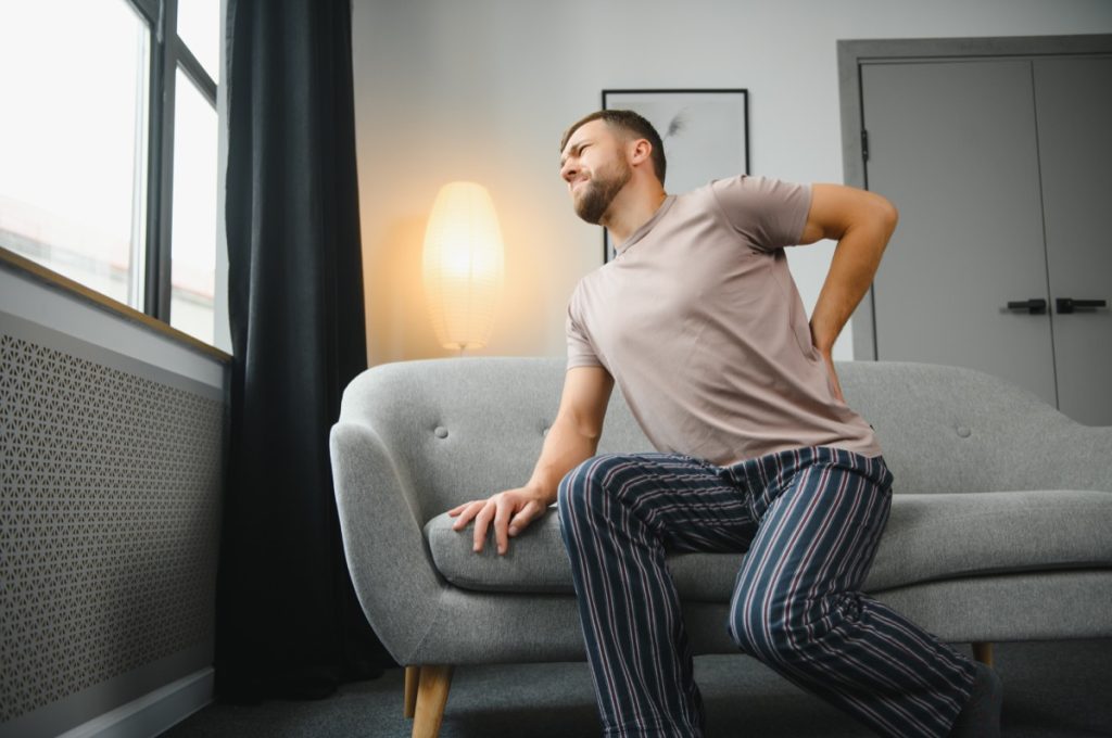 Man sitting on couch holding lower back and looking pained