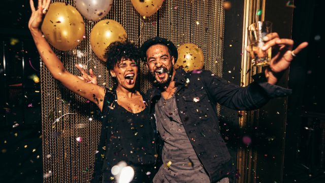 An energetic young couple celebrating the holidays with gold balloons and confetti around them.