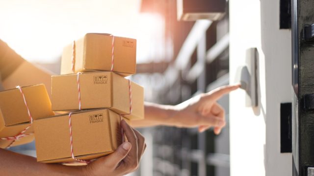 Delivery man holding parcel boxes and ring the doorbell on the client’s door in the morning background.