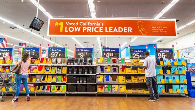 People shopping for back to school items in one of the Walmart stores; Banner advertising the low price leader status in California displayed above