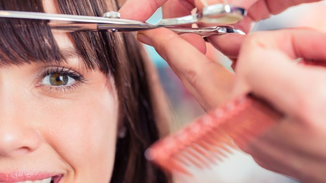 Close up of a brunette woman getting her bangs trimmed.