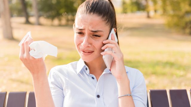 A young brunette woman cries while talking on her cell phone on a park bench.