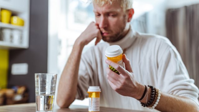 A man is sitting and holding head in his hands while thinking and looking at the pill bottles