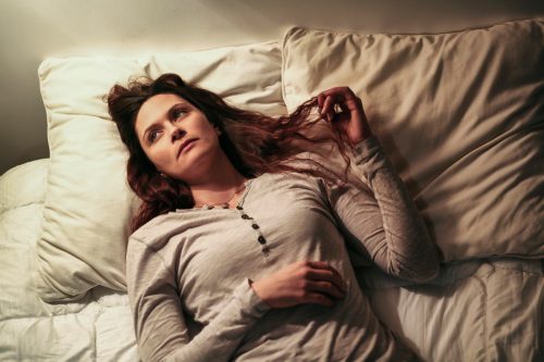 Bored woman lying in bed and playing with her hair