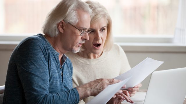 A senior couple looking at a letter with a shocked expression on their faces