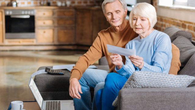 A senior couple sitting on the couch and opening and envelope