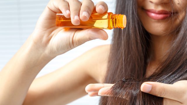 woman with long dark hair applying hair oil
