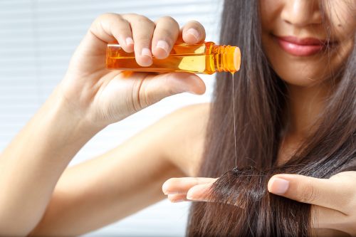 woman with long dark hair applying hair oil