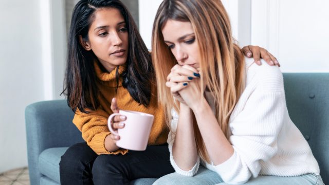 A young woman comforting her sad friend while sitting on the couch.
