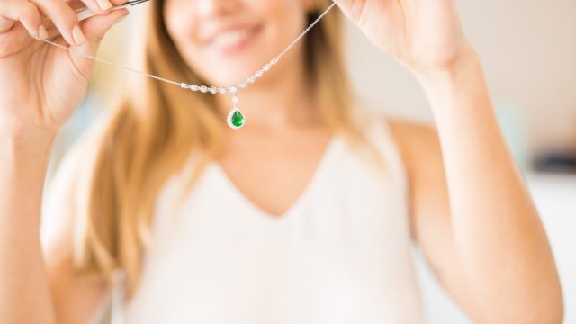 Close up of a woman holding up an emerald and diamond necklace