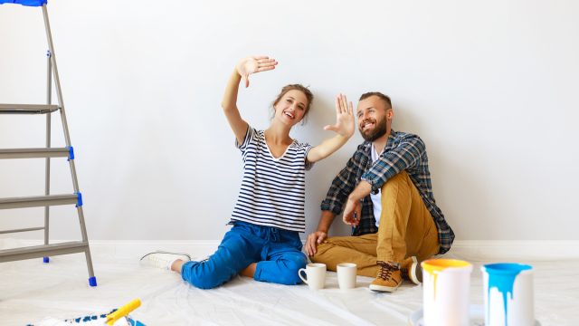 A young couple sits on the floor to take a break from painting a room
