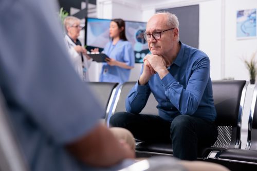 Stressed tired senior patient sitting on chair in hospital lobby while waiting for specialist doctor to start medical examination during checkup visit consultation.