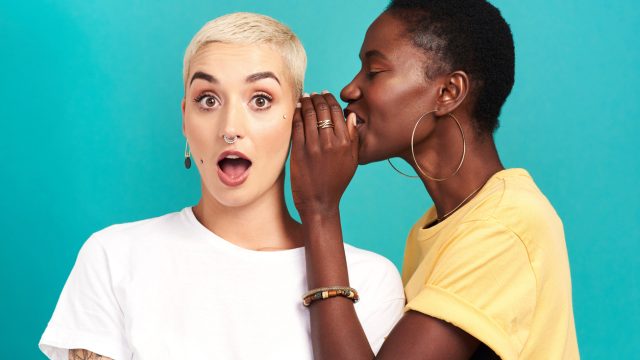 Studio shot of a young woman whispering in her friend’s ear