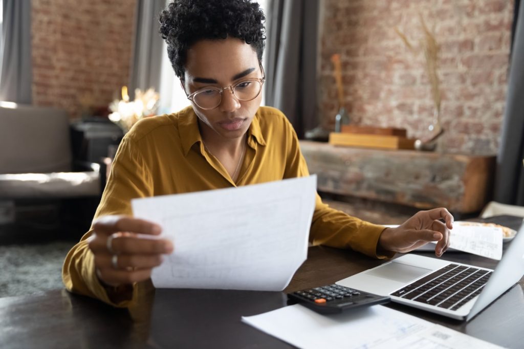 Young woman sitting at desk with laptop and calculator, looking intently at a tax form