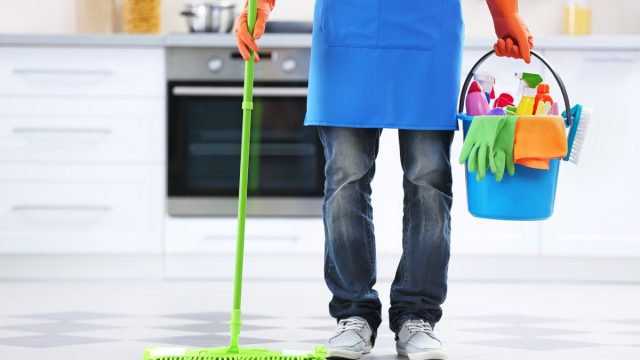 Man holding mop and plastic bucket with brushes, gloves and detergents in the kitchen