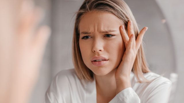 Mirror reflection of upset young lady looking at mirror and touching her forehead, having oily or dry skin problem, first wrinkles concept, bathroom interior