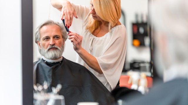 Female mid adult hairstylist using a comb to style her grey hair client in a hair salon.