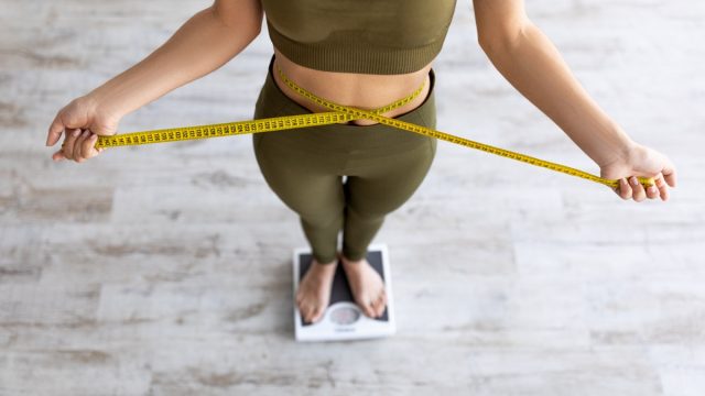 woman measuring waist while standing on scale