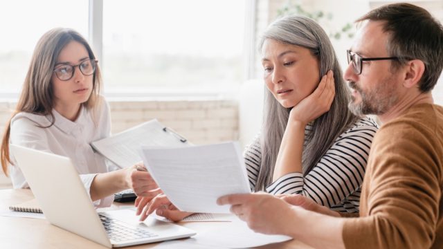 Consultant financial advisor specialist dealing with mature couple clients, discuss health insurance, bank account history. Middle-aged family spouses customers consult with relator broker.