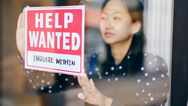 A small business owner, putting up a help wanted sign in her store window.