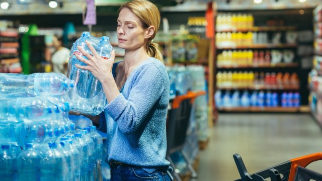 A young woman buys pallets of water in a supermarket. He takes it in his hands, packs it in a cart. Panic during a pandemic, quarantine.