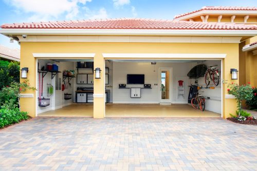 Looking into a well-organized three-car garage attached to a yellow house with terra cotta roof.