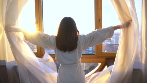 woman in the morning looking out the window and the bright sun shines.