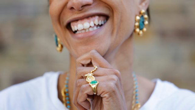 Close up of a smiling woman wearing gold and turquoise matching earrings, rings, and necklaces
