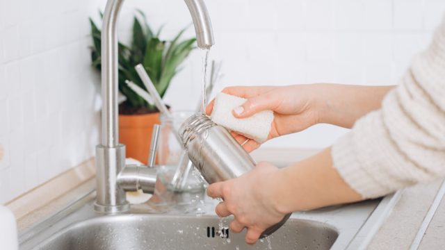 Woman washing a water bottle in kitchen sink