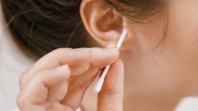 Woman is cleaning ear with a cotton swab