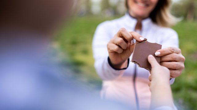 An unrecognizable girl shares chocolate with her mother outdoors