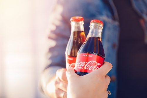 two men cheers one another with glass coca cola bottles