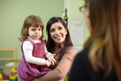 woman holding her young daughter while speaking to her teacher