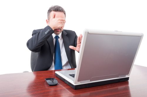 man covering his eyes in front of his computer