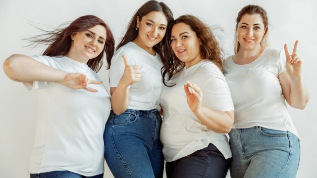 Four female friends posing and giving the peace sign, all wearing white t-shirts and jeans