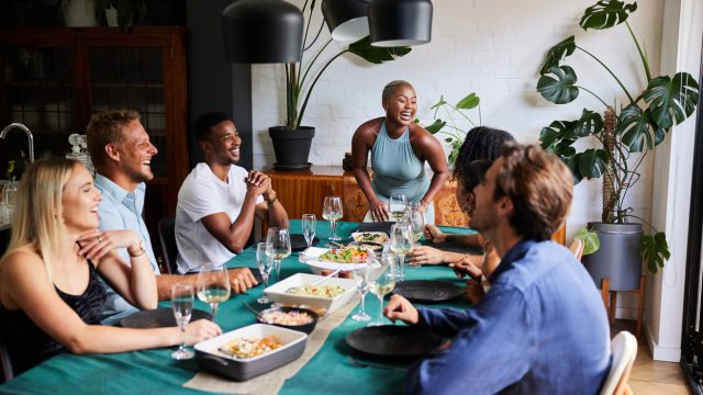 A group of friends sitting around a table at a dinner party while their host begins to serve food