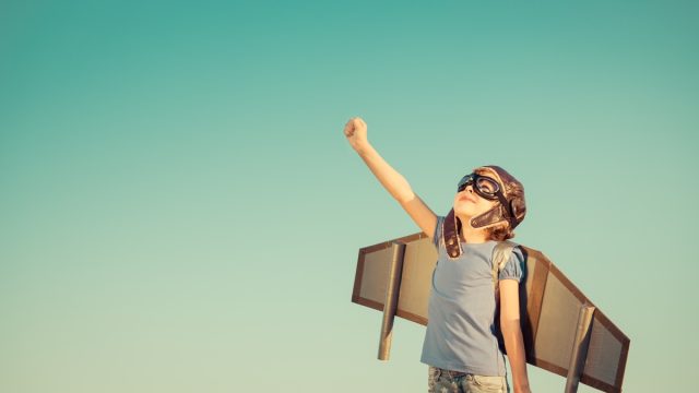 Happy child playing with toy wings against summer sky background.