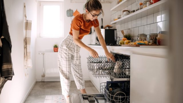 Young woman putting dishes in dishwashing machine