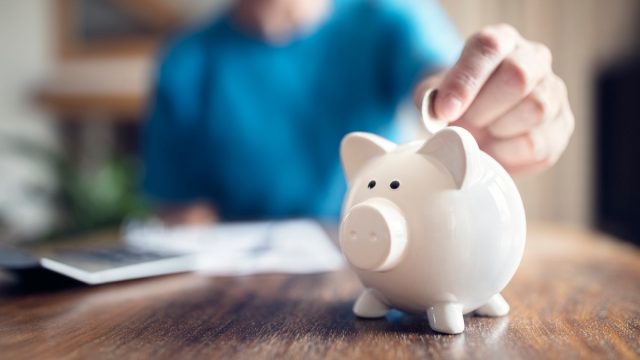 Close up of a person putting a coin into a white piggy bank