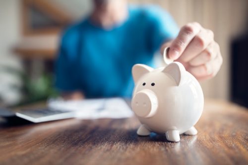 Close up of a person putting a coin into a white piggy bank