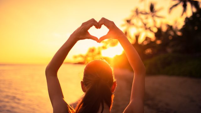 woman making a heart shape with her hands at sunset