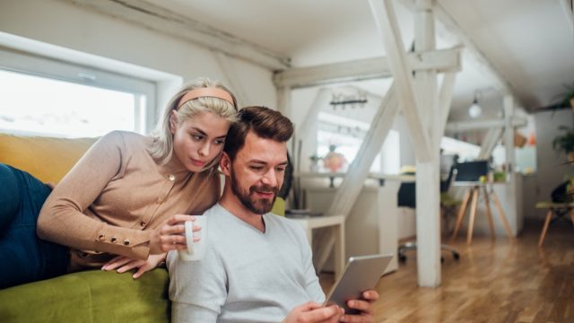 Happy young couple working from home, using digital tablet