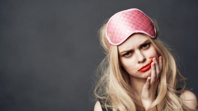 young woman in pink sleep mask with makeup on and smeared lipstick