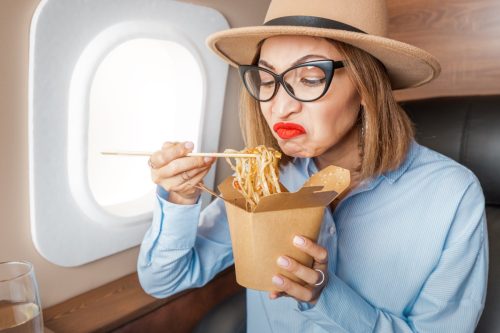 woman on plane looking displeased eating a cup of noodles