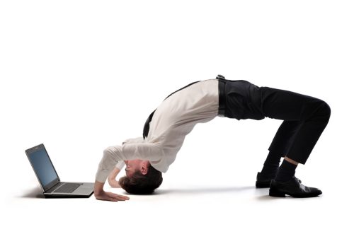 man doing a backbend and looking at his laptop upside down