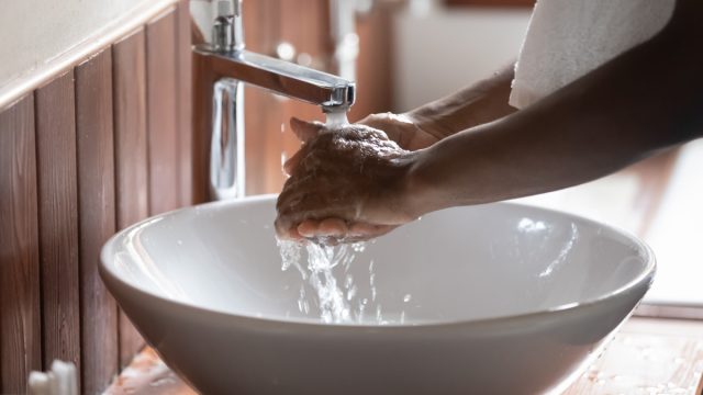 Crop close up of black man washing hands in water from tap