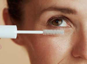 Close up of a woman applying a clear mascara gel in a white tube to her eyelashes