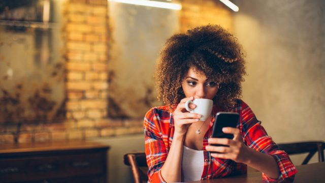 Woman Drinking Coffee While on Her Phone